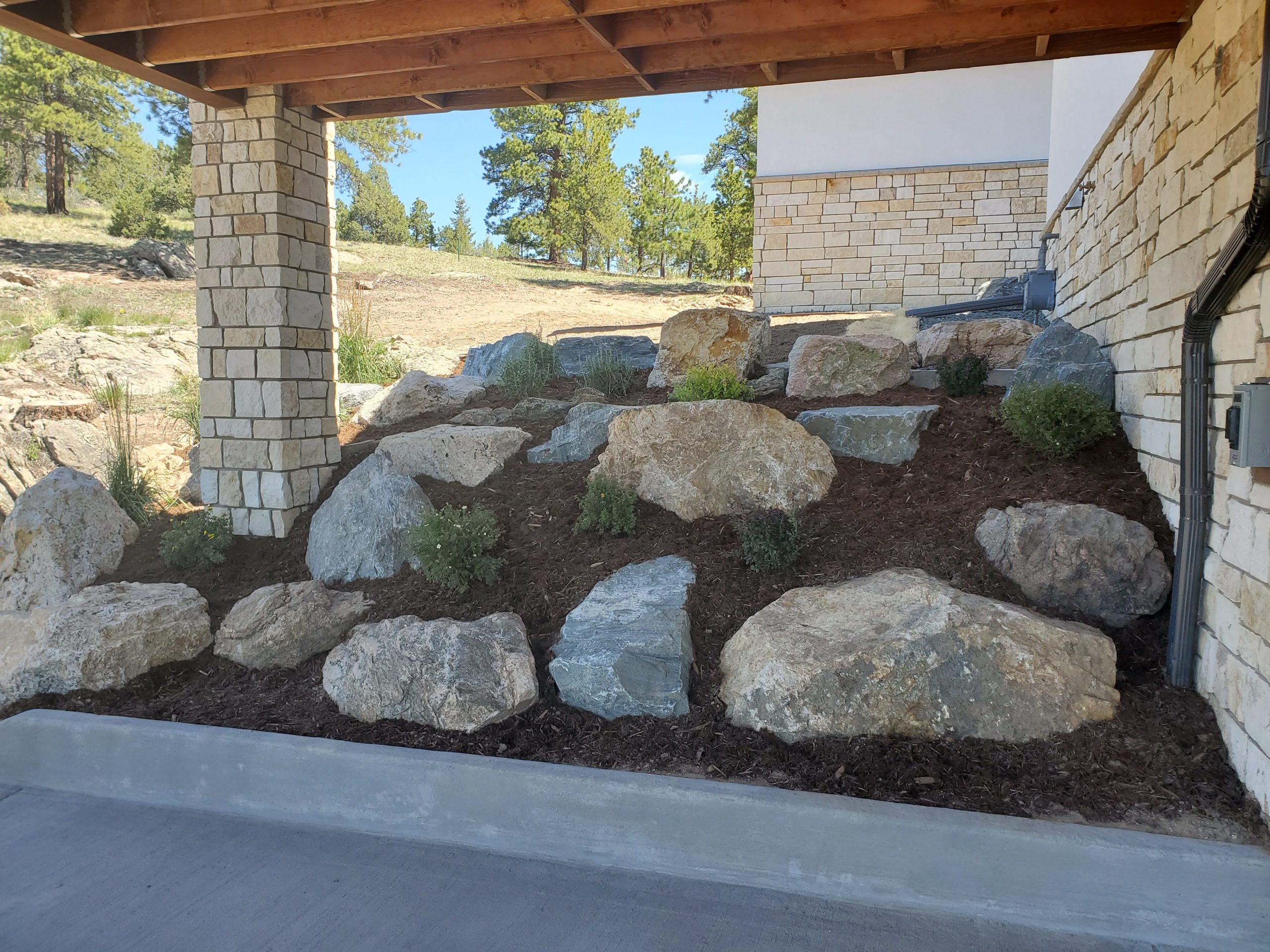 Landscaped hill next to house with large boulders and bushes