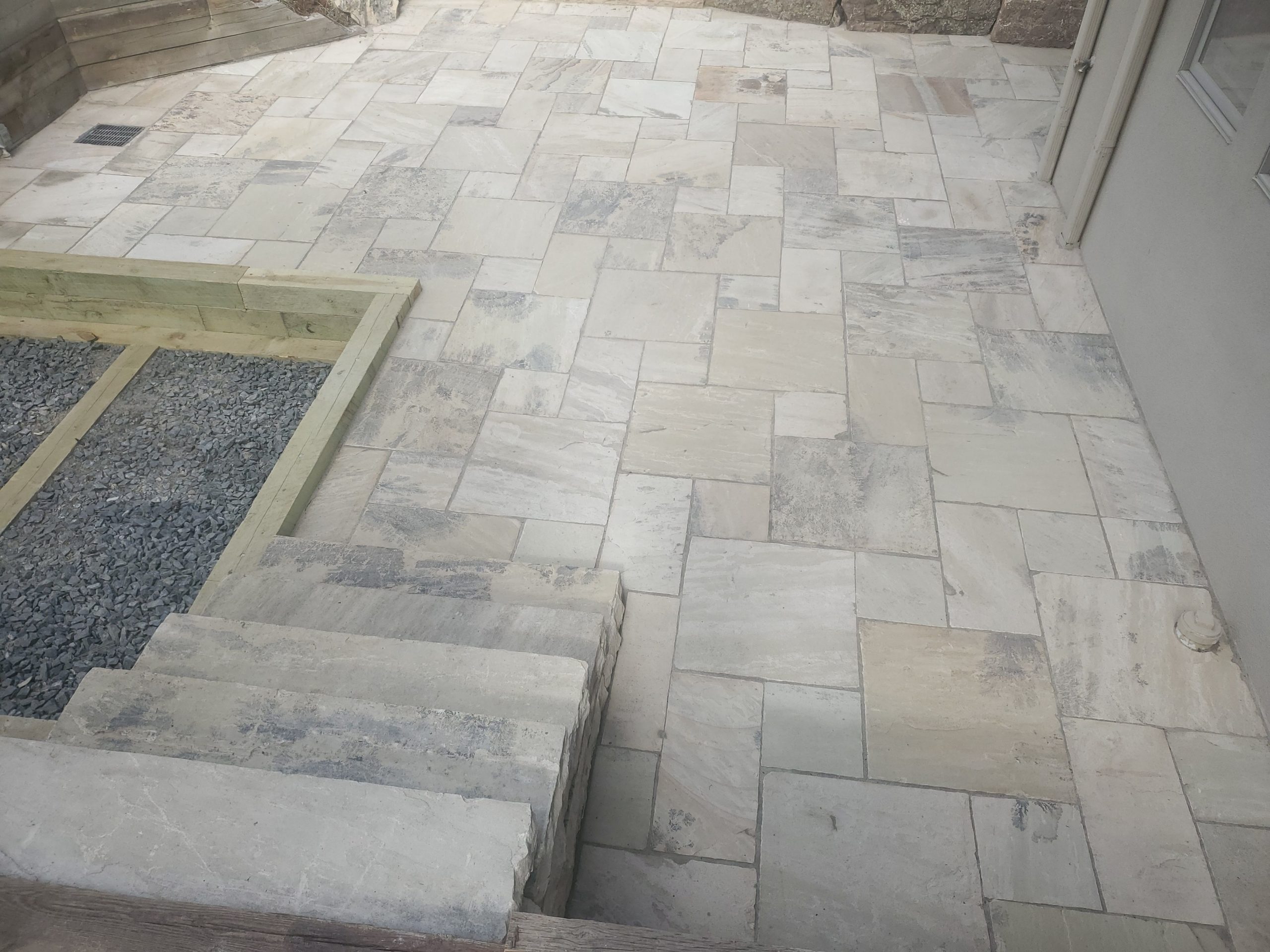 Square stone patio with inset garden beds next to staircase
