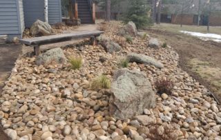 kidney-shaped river rock space with bench, near entryway staircase to house