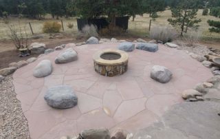 Red rock patio with stone fireplace in center, with large river rock benches