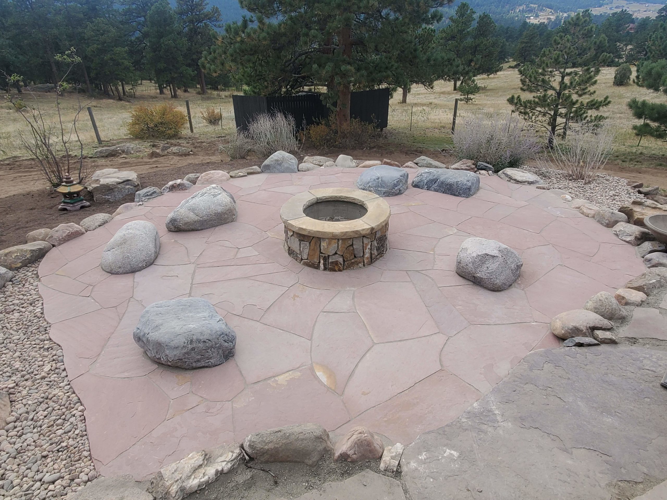 Red rock patio with stone fireplace in center, with large river rock benches