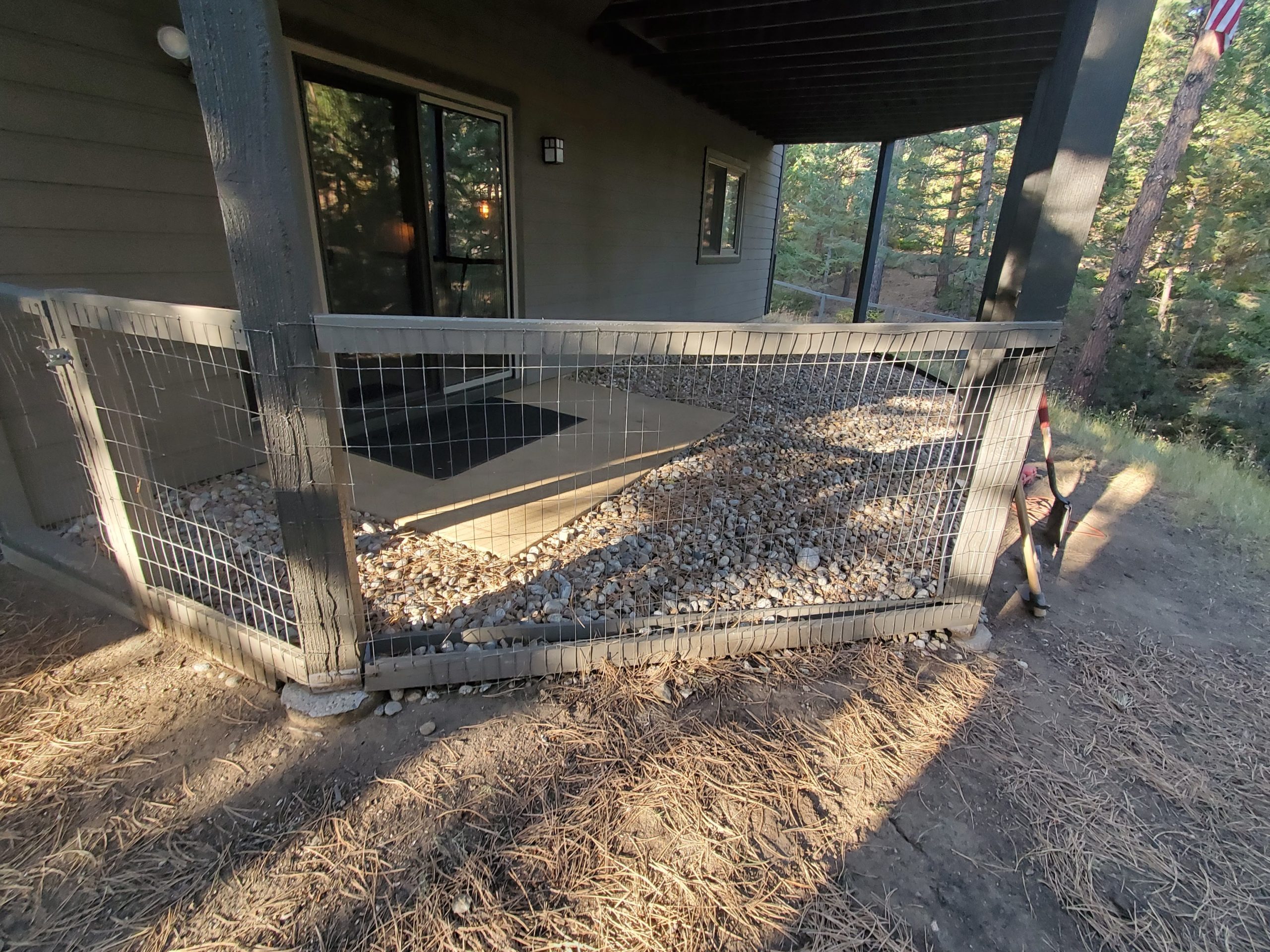 Fenced covered area under deck with river rock