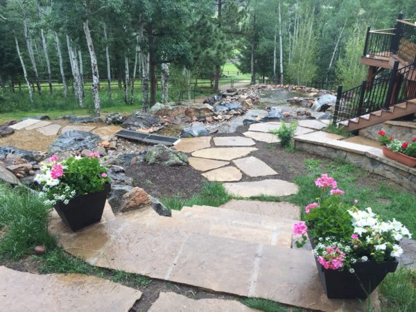 Large backyard in Evergreen, CO with flagstone steps and path, leading to mid-size pond and waterfall