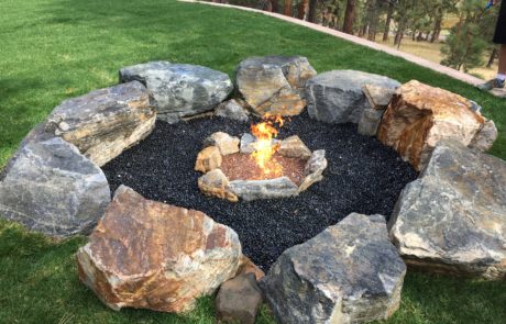 Lit fireplace surrounded by black gravel, with larger rocks beyond that for seating