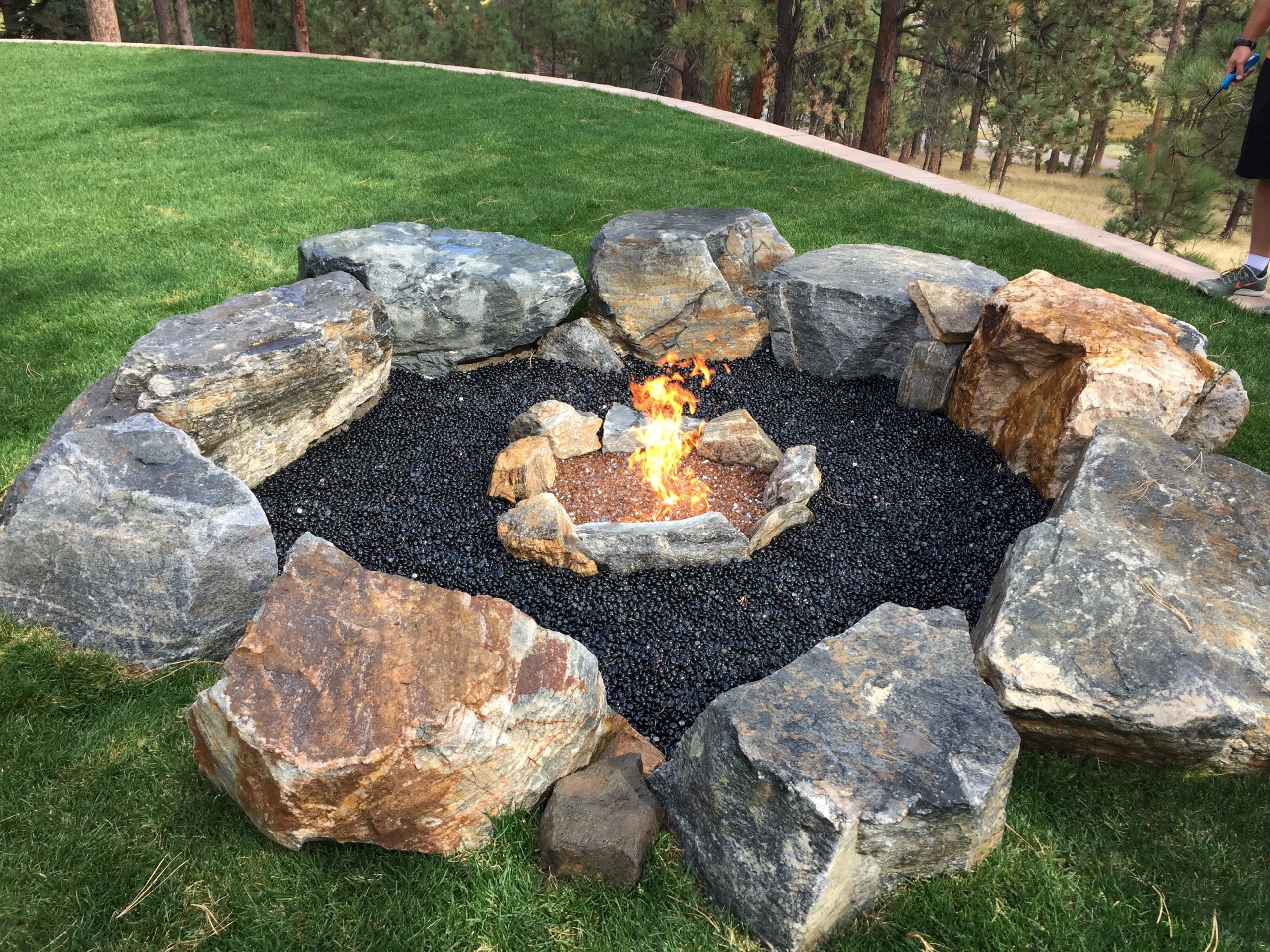 Lit fireplace surrounded by black gravel, with larger rocks beyond that for seating
