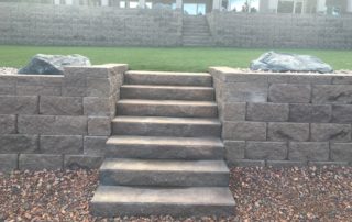 Stone staircase with retaining wall leading to grass yard with second staircase and retaining wall in background