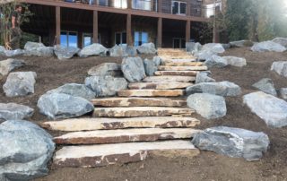 Large gray boulder surround stone staircase to back of house