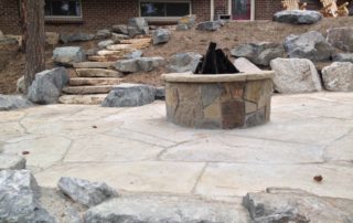 Stone fireplace in center of flagstone patio with stone staircase in background