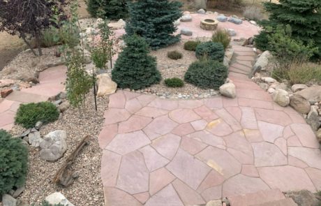 Overview of backyard with landscaped trees and bushes, with path leading to stone fireplace