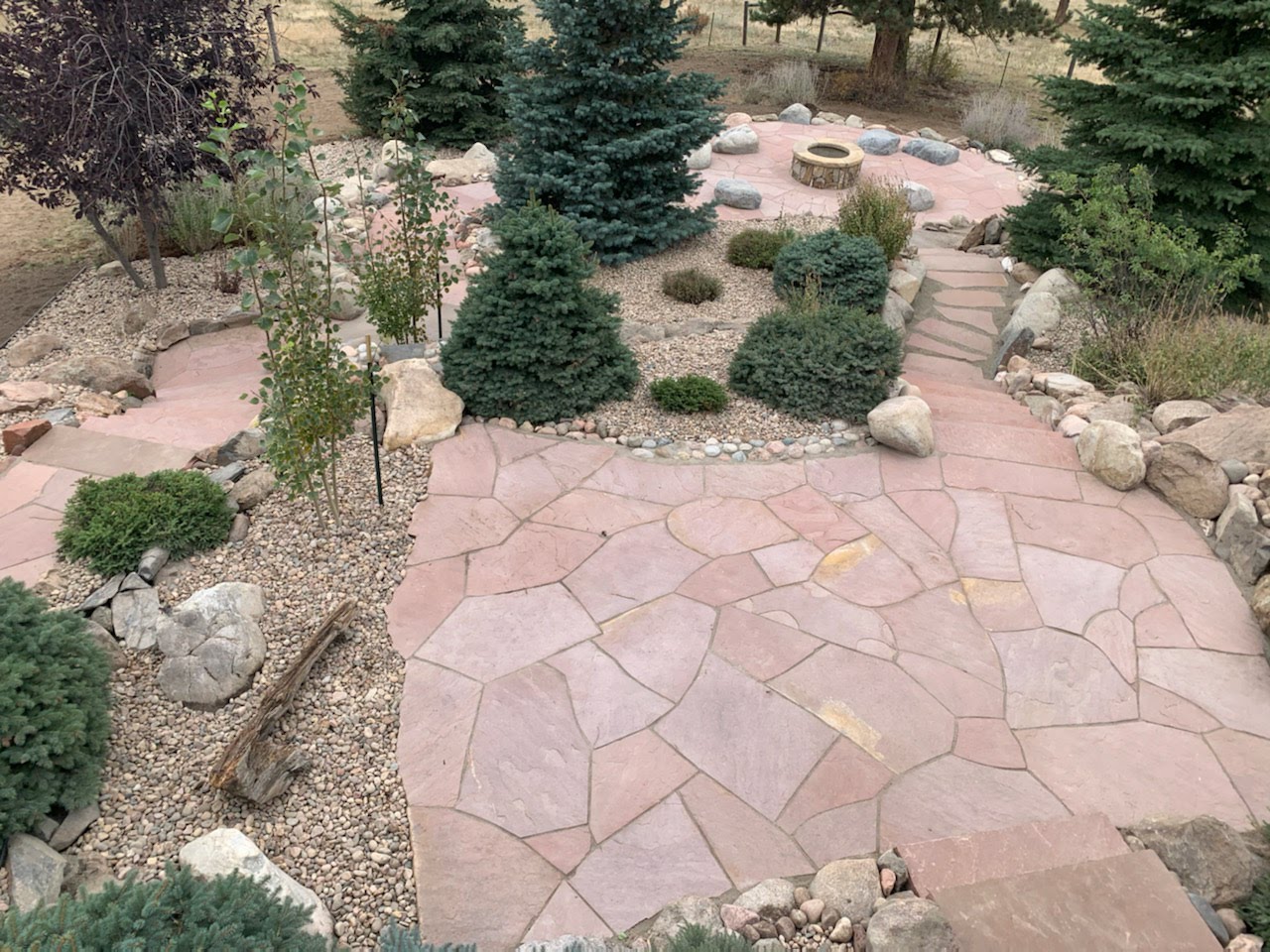 Large outdoor space complete with red flagstone paths, landscaped trees, and fireplace