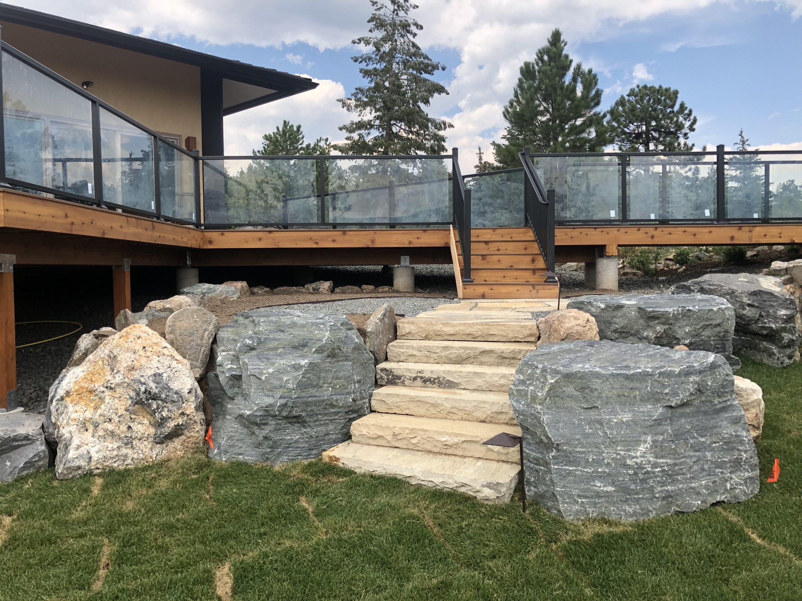 Large boulder surround stone staircase leading to deck with black railings and glass