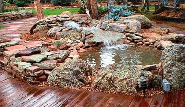 Wooden deck next to small pond and waterfall, lined with rocks of various size