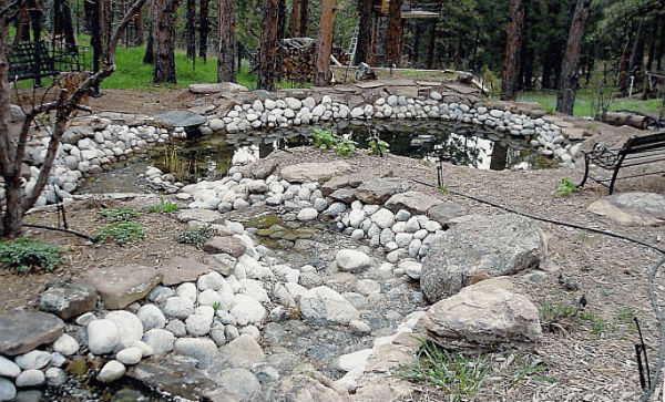Large water feature comprised of river rock, leading to pond and nearby bench